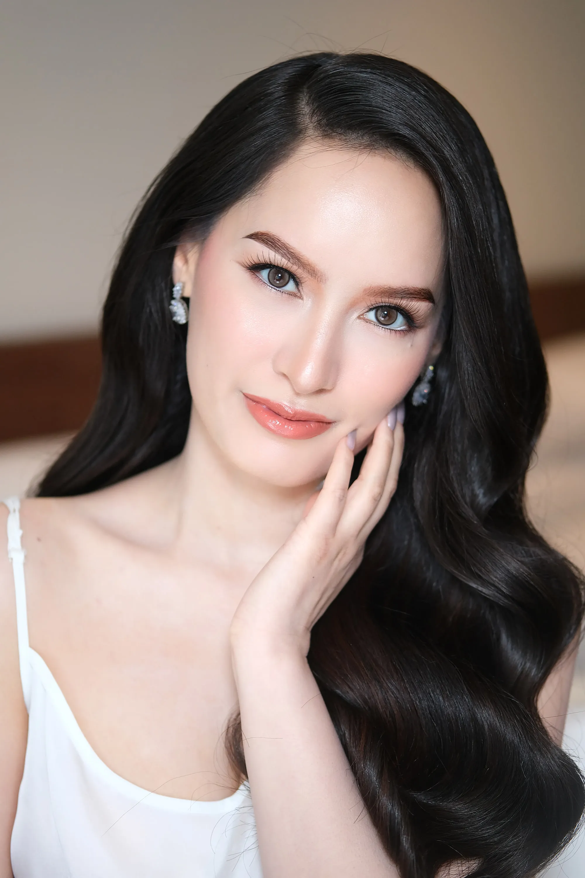 The same sculpted bridal look seen closer, with the hand raised to the cheek and long dark waves loose.