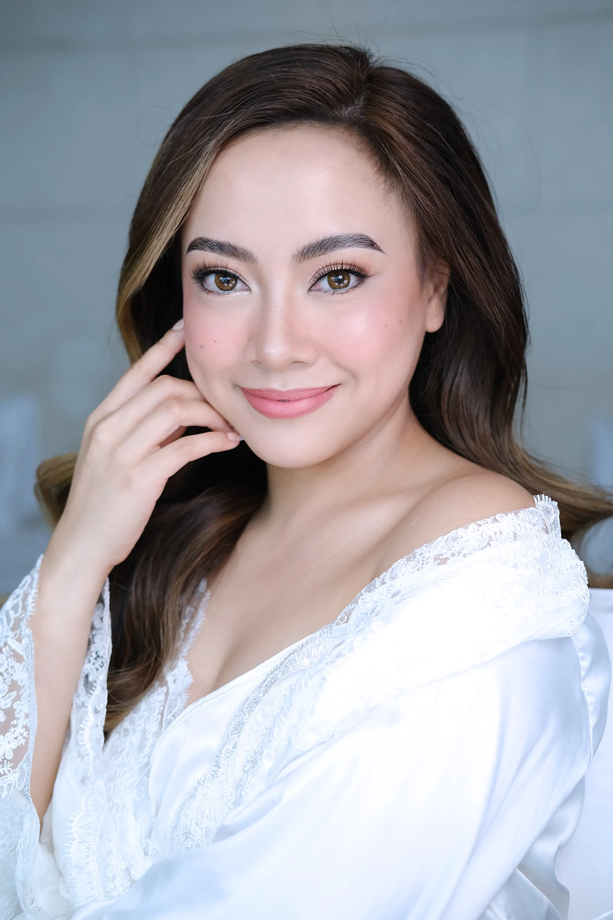 Bridal make-up with a natural skin finish and a soft pink lip, worn with a side part and a sheer white sleeve.